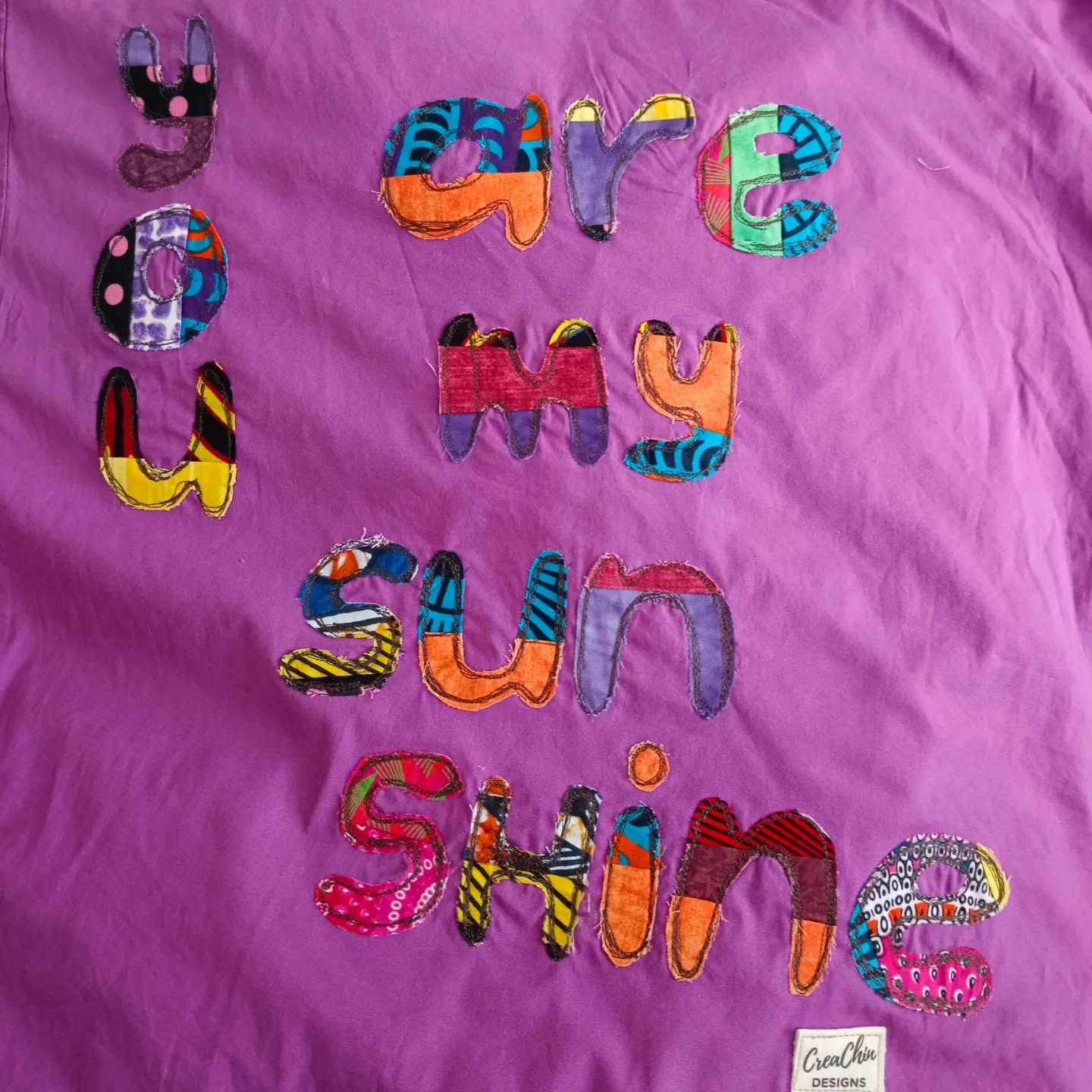 Visible mending on a purple dress with appliqué letters