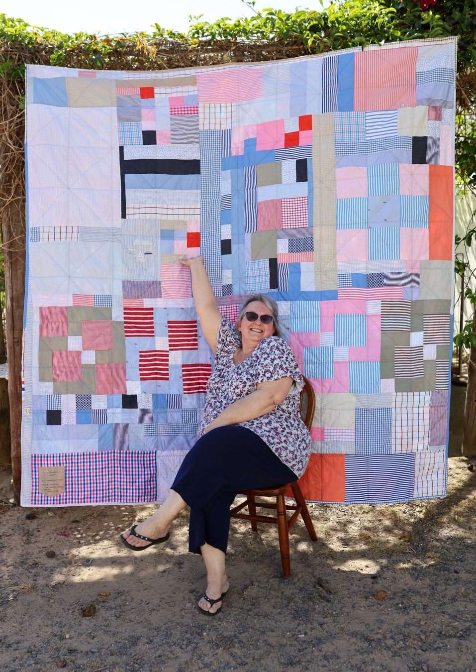 The back of a memory quilt, pieced from shirt fabric instead of one plain piece, with its maker sitting in front of it